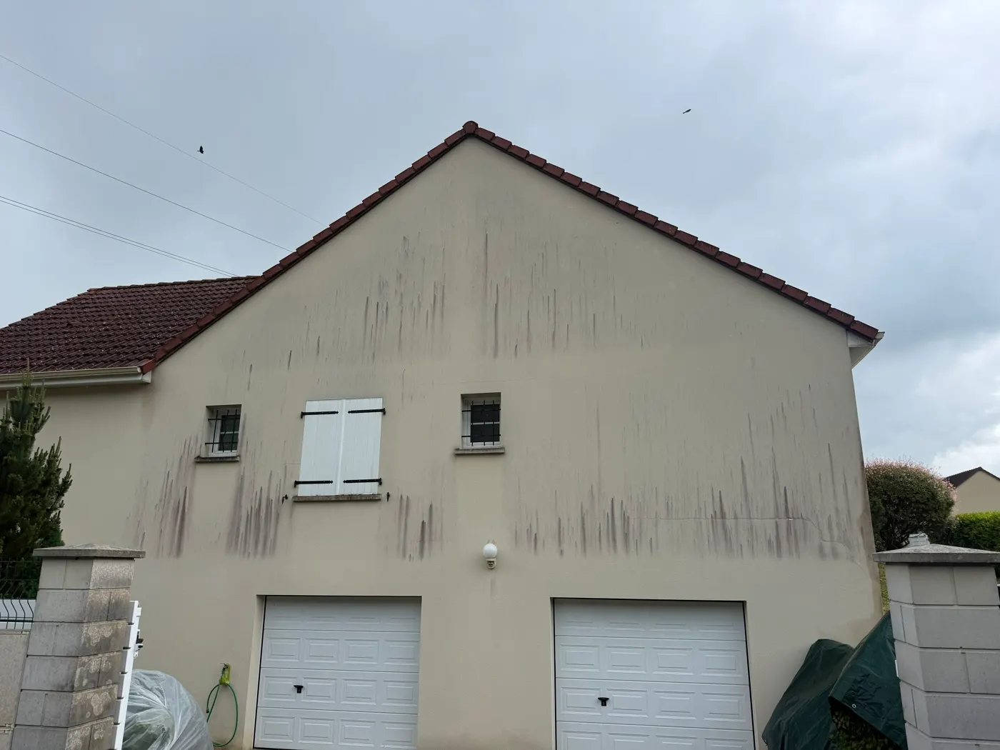Le pignon crépi d’une maison, strié de coulures sombres sous la rive de toiture et le long des descentes.